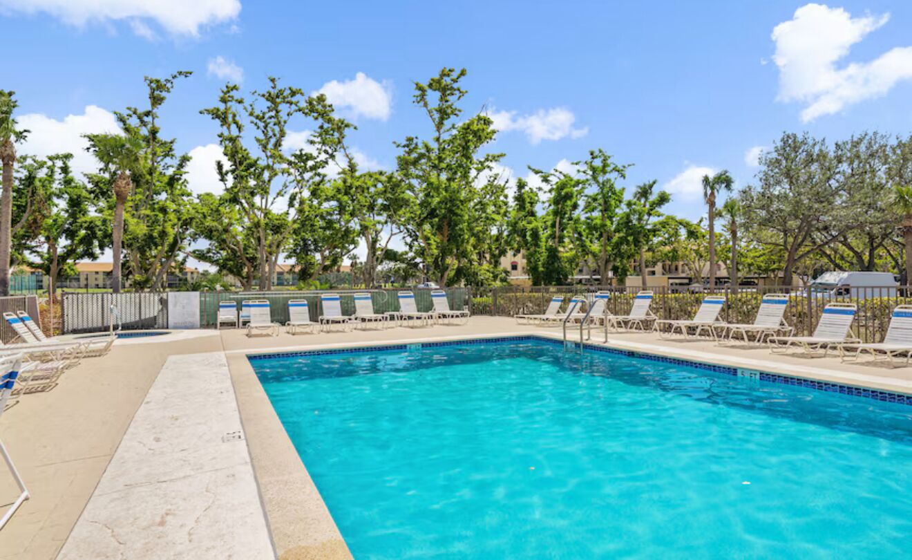 A rectangular swimming pool with clear blue water, surrounded by lounge chairs and trees.