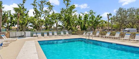 A rectangular swimming pool with clear blue water, surrounded by lounge chairs and trees.