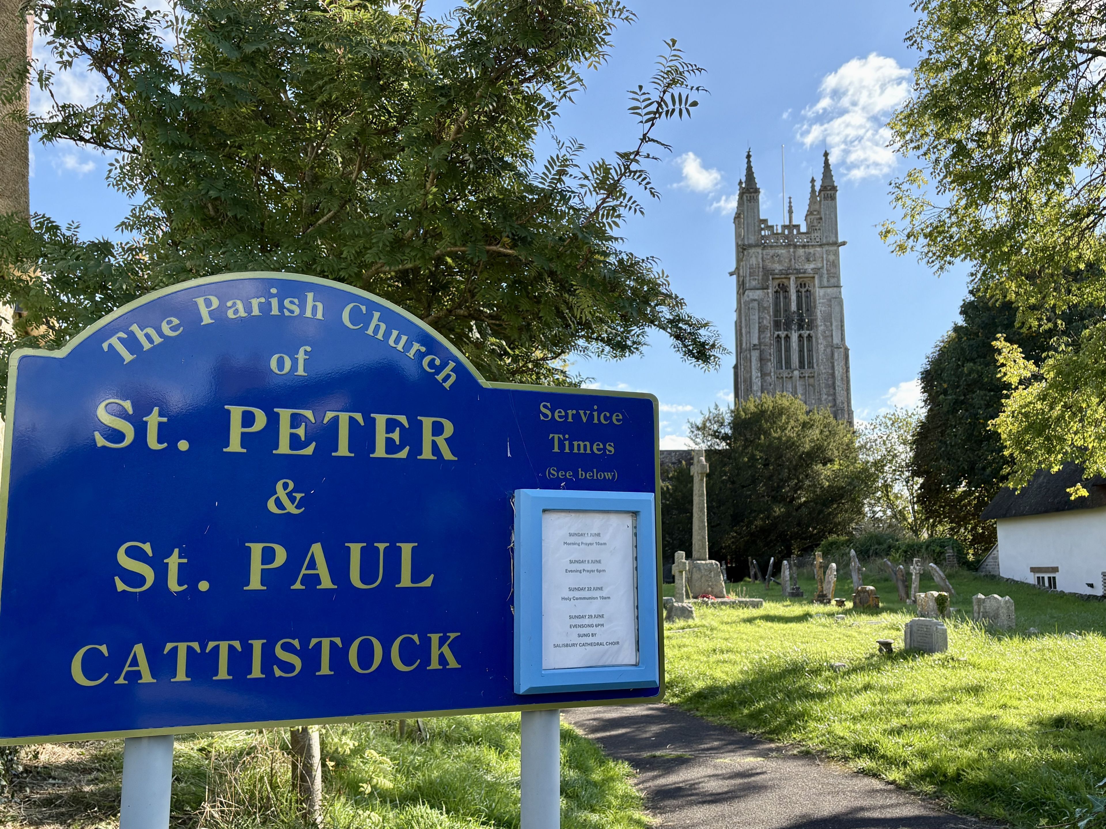 A sign for The Parish Church of St. Peter & St. Paul Cattistock with a service times board beside it.