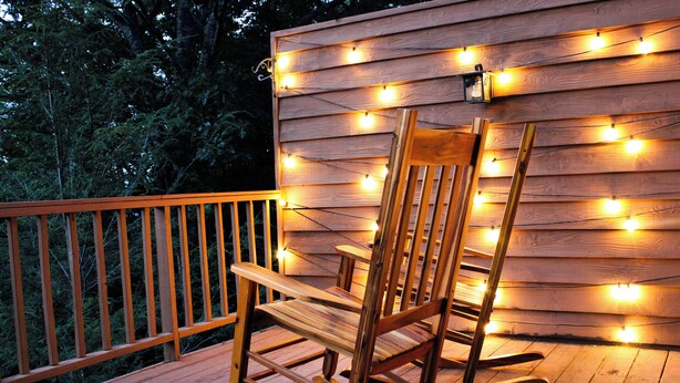 A wooden rocking chair on a deck with a string of lights.