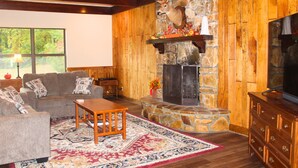 A cozy living room with a stone fireplace, wooden walls, a sofa, and a television.