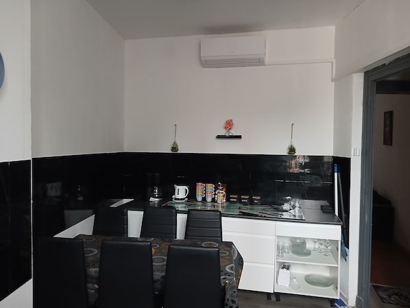 Una cocina compacta con cubierta negra, armarios blancos y un pequeño comedor con sillas.