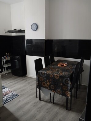 A dining area with a table set for four, a clock on the wall, and a black and white backsplash.