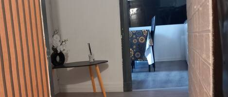 Un pasillo con piso de madera, una pequeña mesa con un florero y vista a una habitación con mantel estampado.