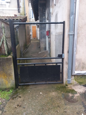 Una puerta de metal con diseño de malla, una base de hormigón y una tubería metálica a la derecha.