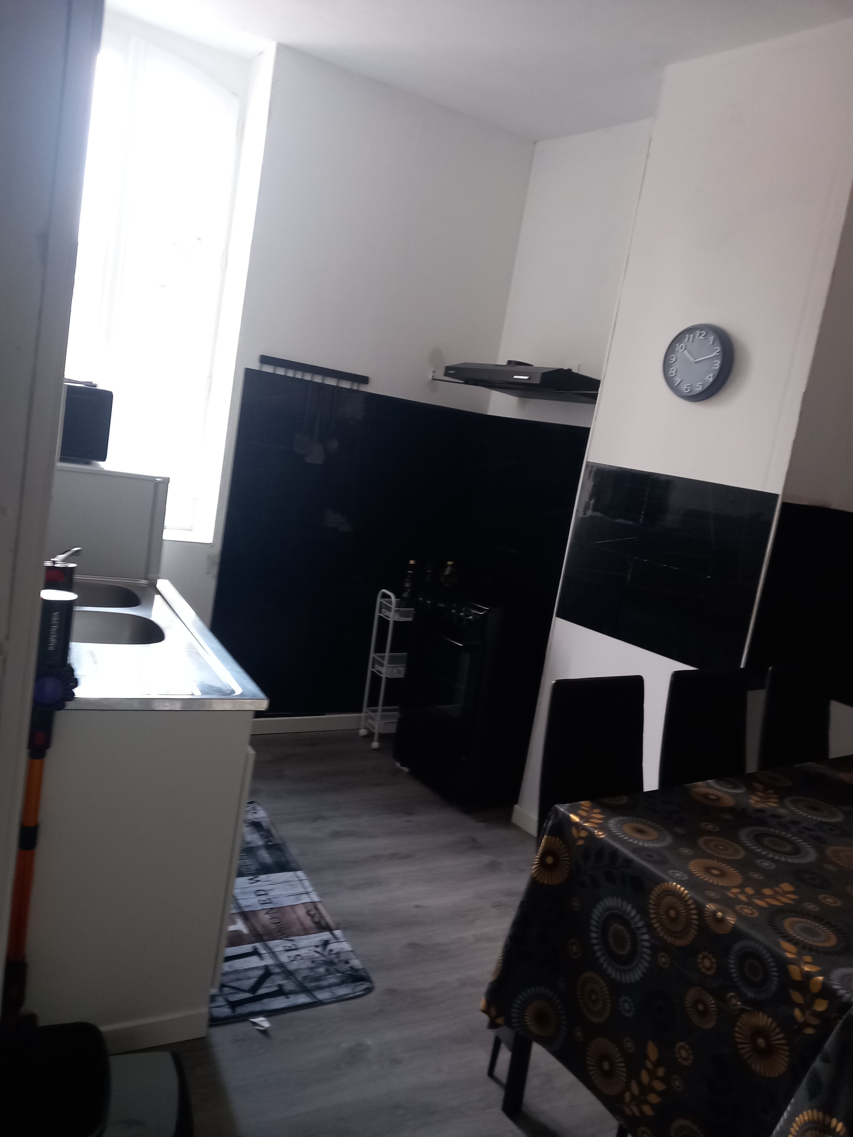 A compact kitchen with a sink, a microwave, and a clock on the wall.