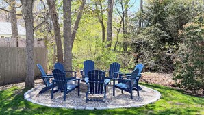 Un espace extérieur circulaire aménagé avec des chaises Adirondack et une table, entouré d’une clôture en bois et d’arbres.