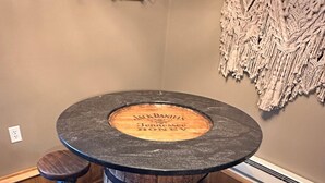 A round wooden table with a central barrel, four stools, and a macrame wall hanging.