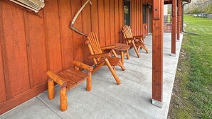 A covered outdoor seating area with wooden Adirondack chairs and a concrete floor.