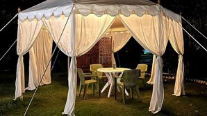 A large, white tent with a table and chairs inside, set up on a grassy area at night. - Riyasat Panthera (Bali)
