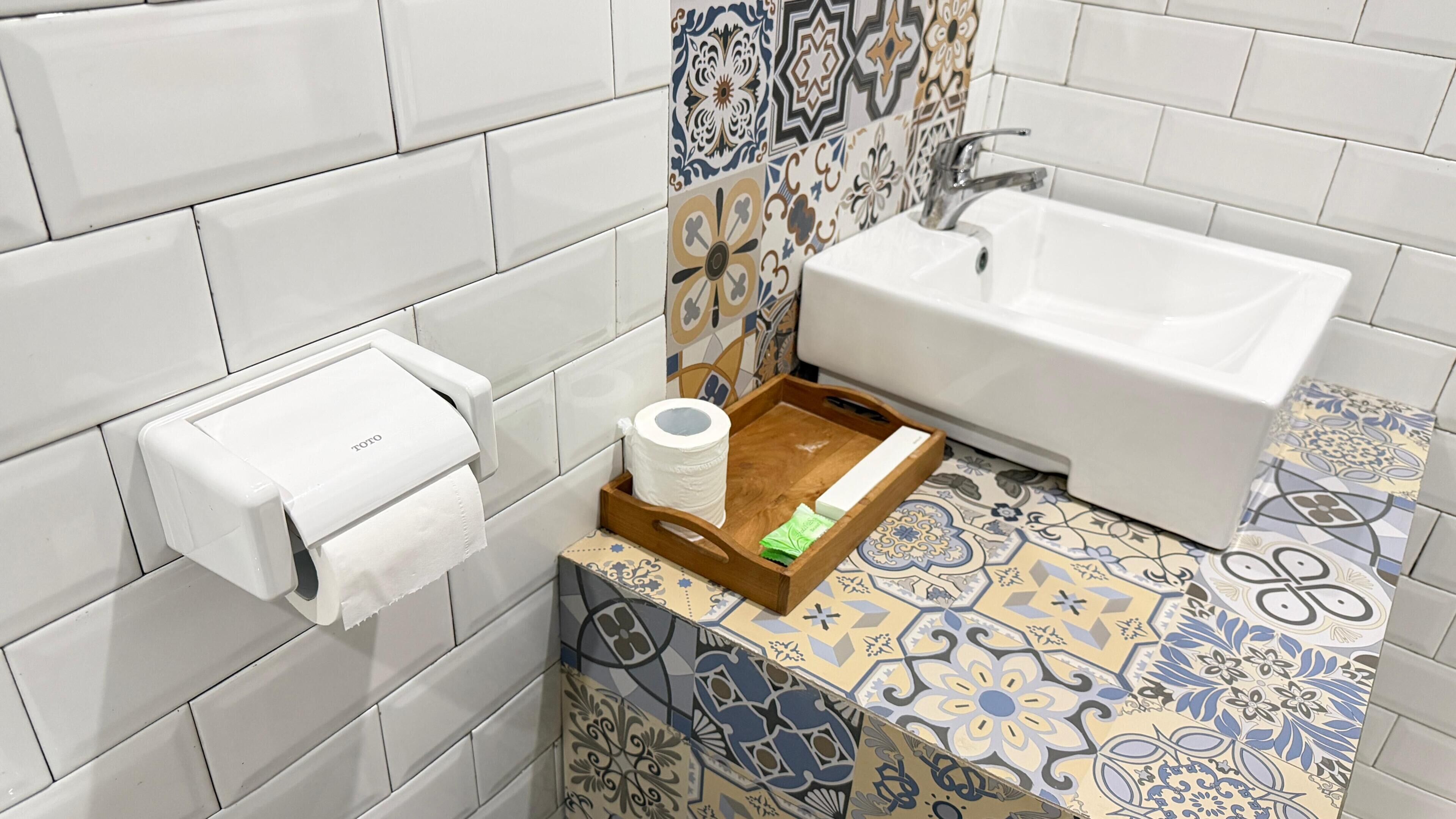 A bathroom with a toilet paper dispenser, a hand dryer, and a tray with toiletries.