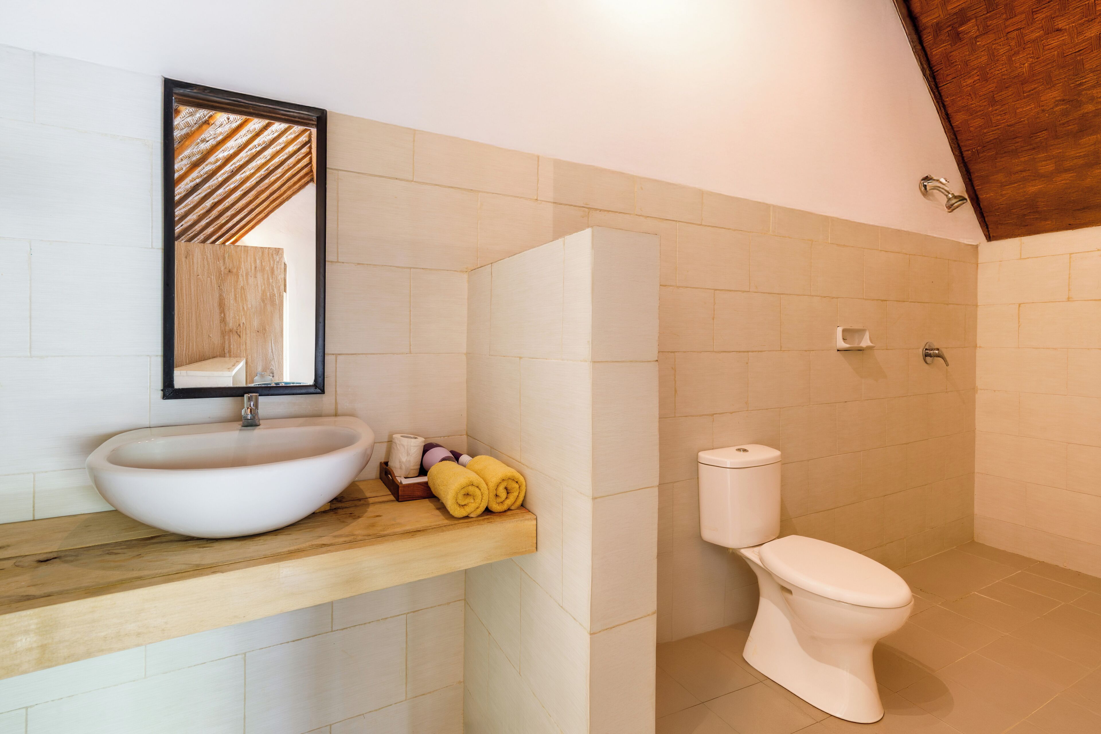 A bathroom with a wooden vanity, a white sink, a toilet, and a mirror.