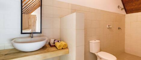 A bathroom with a wooden vanity, a white sink, a toilet, and a mirror.