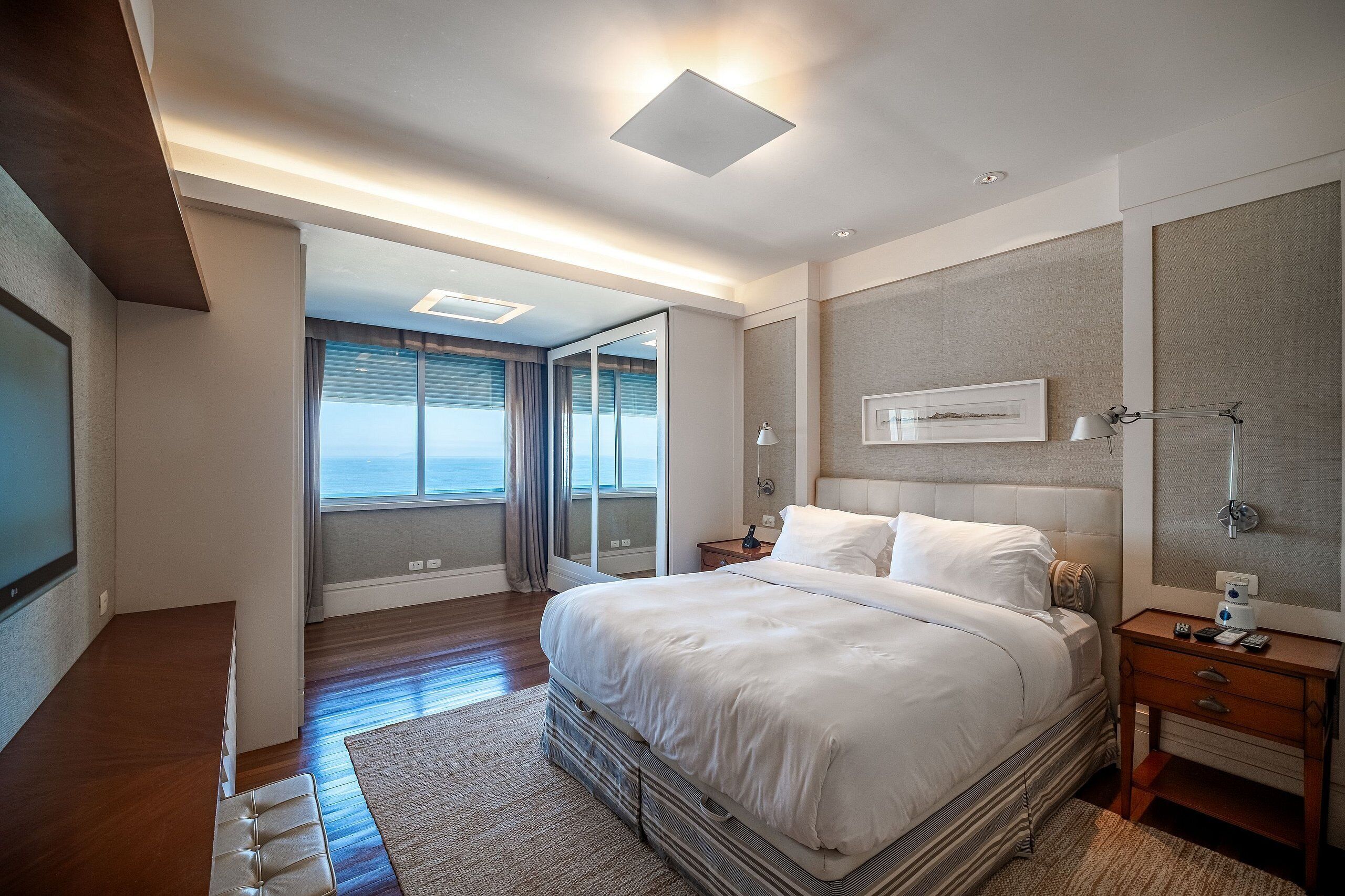 A modern hotel room with a large bed, a desk, and a view of the ocean through the sliding glass door.