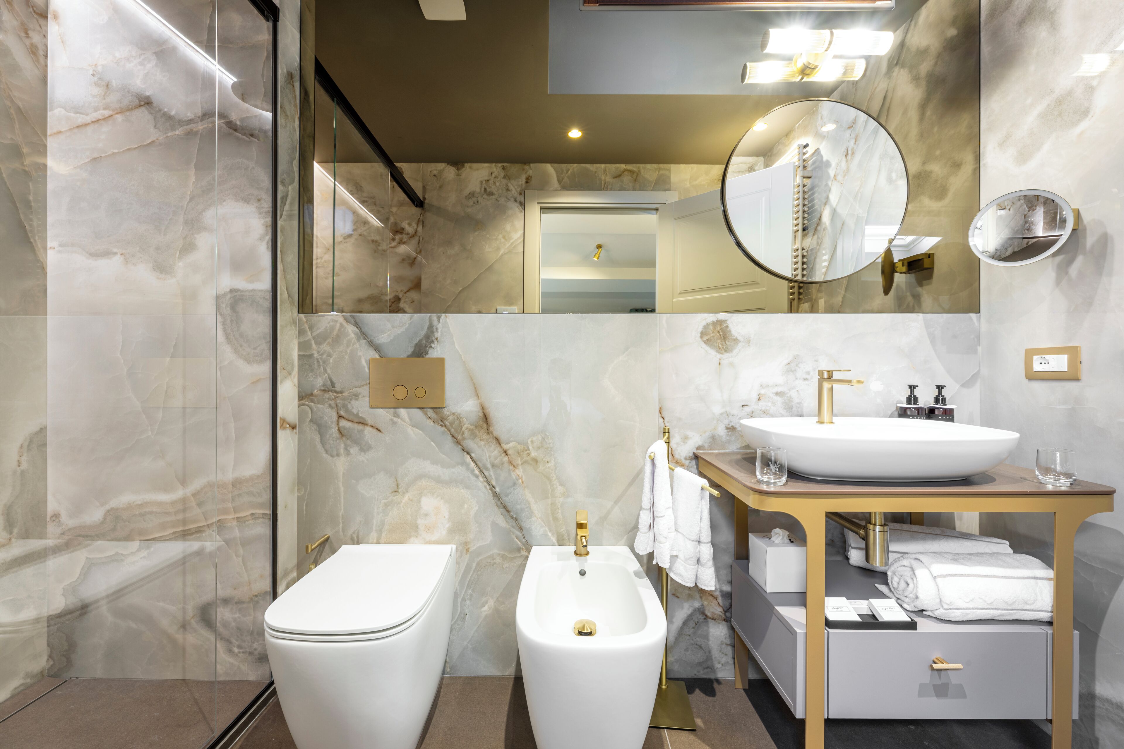 A modern bathroom with a white toilet, a bidet, a sink with a gold faucet, and a vanity with a mirror.