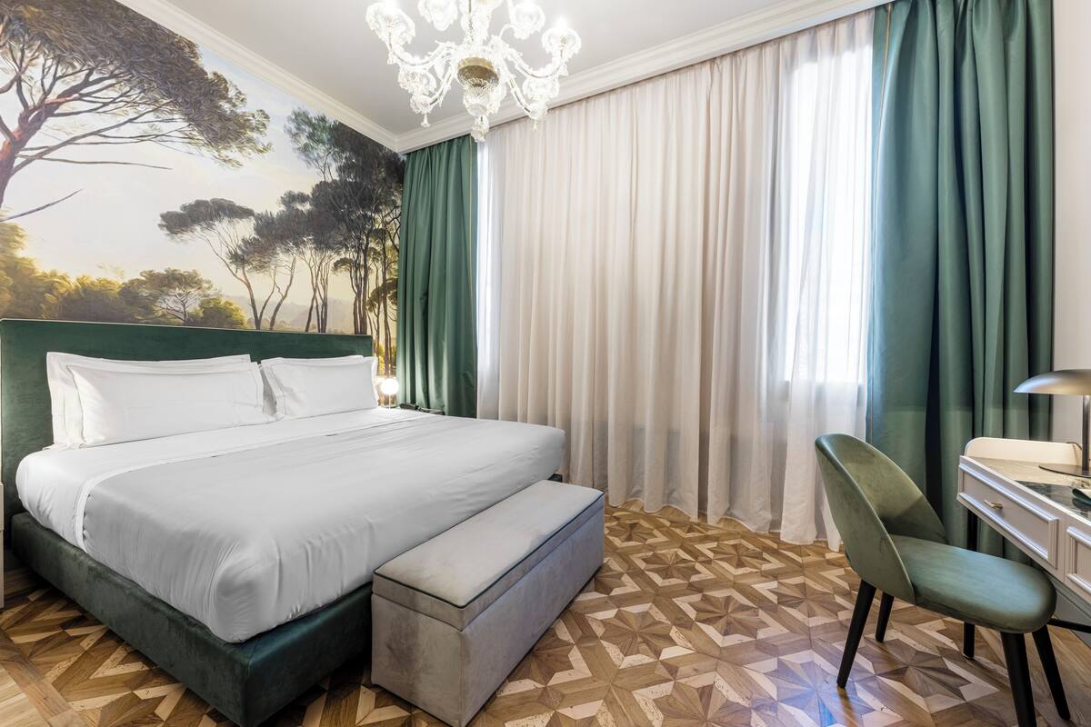 A hotel room with a bed, a desk, a chair, and a chandelier.
