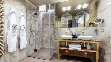 A modern bathroom with a glass-enclosed shower, two sinks with gold fixtures, and marble walls.