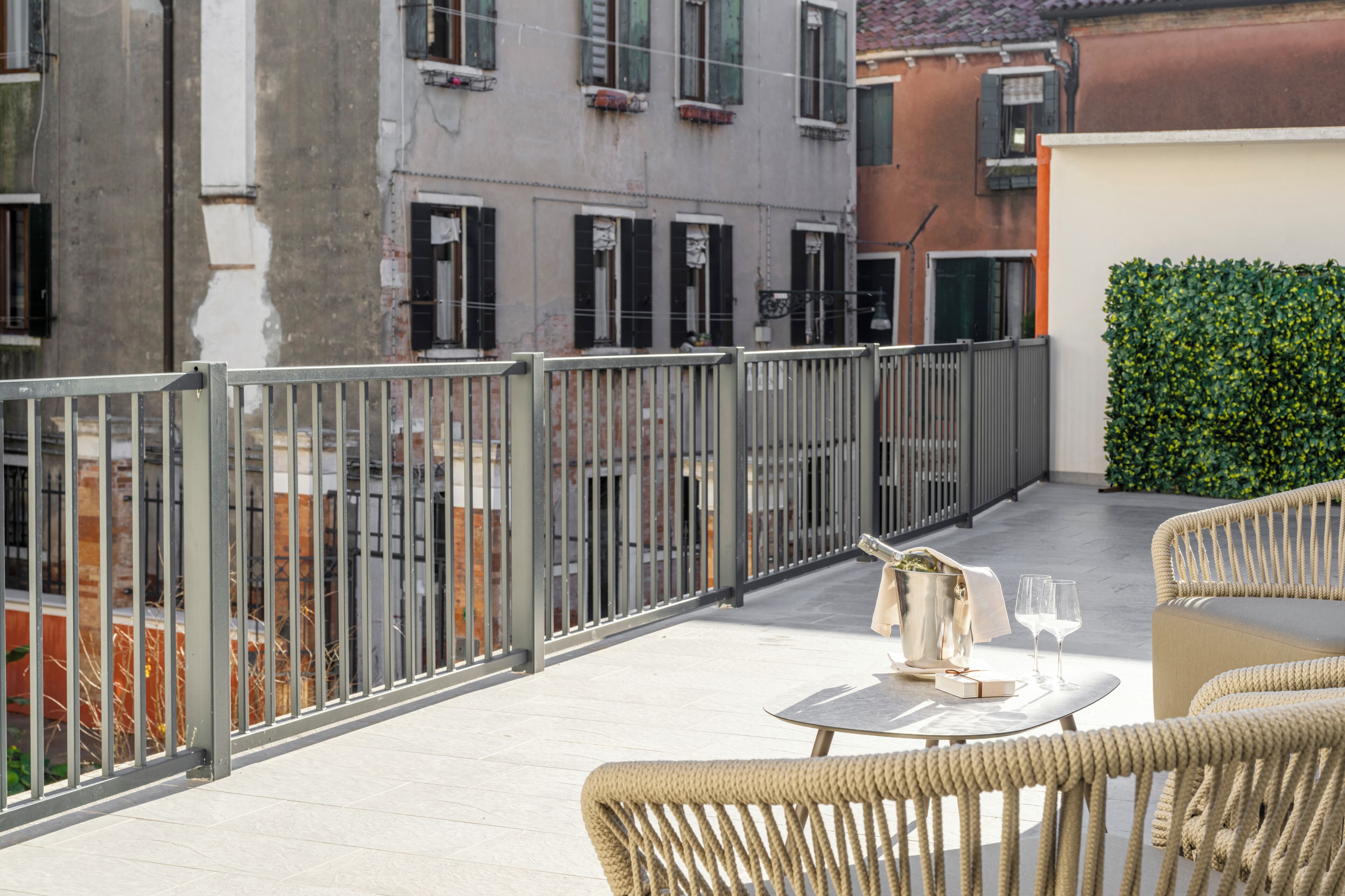 Ein Balkon mit Korbmöbeln, einem Tisch mit Flasche und Gläsern sowie einer Hecke.