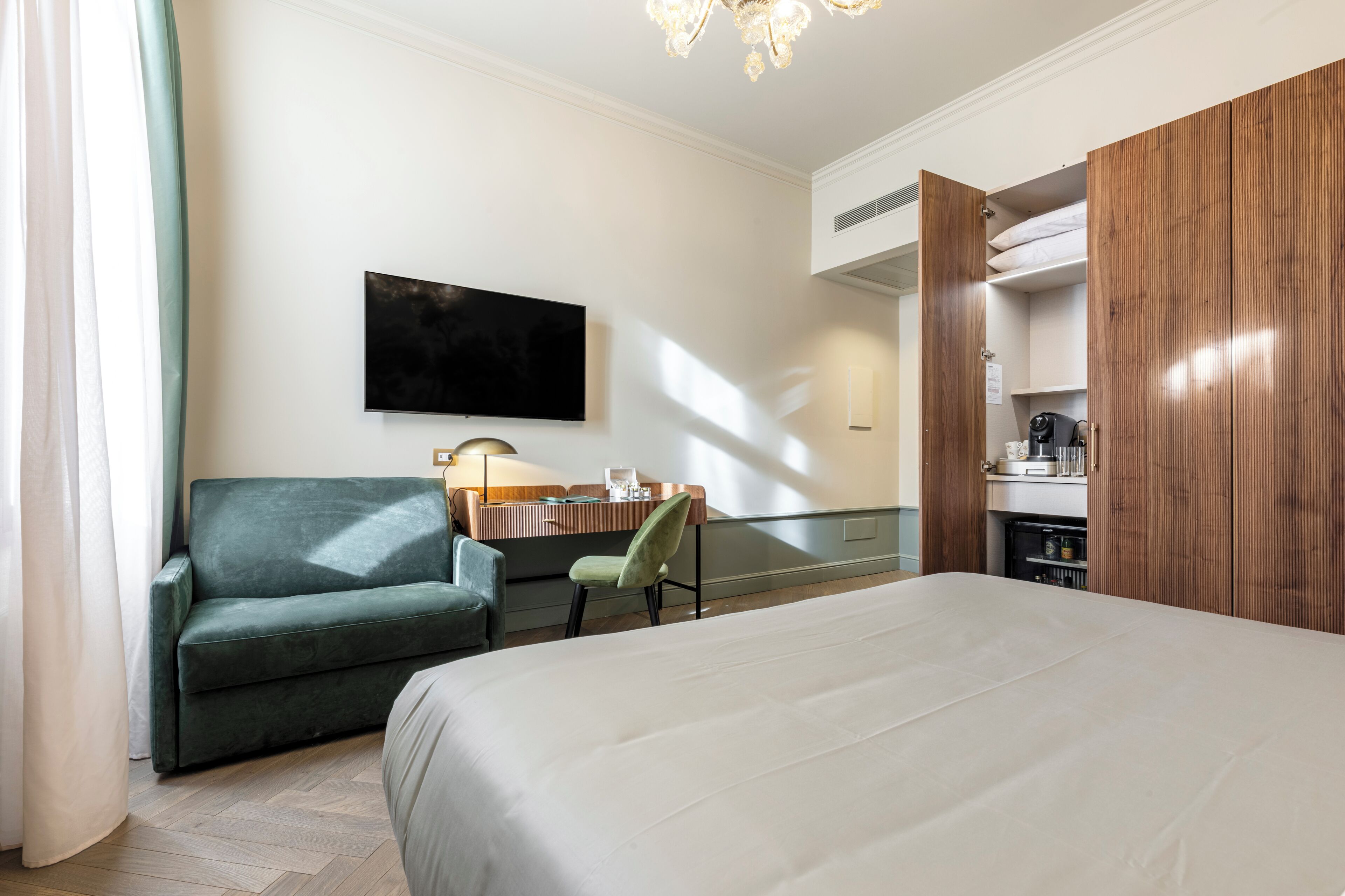 Habitación de hotel con cama, sofá, escritorio, televisor y armario.