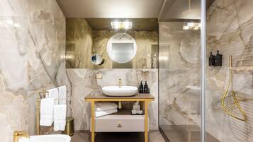Un baño moderno con pared de mármol, un espejo redondo, un lavamanos blanco y un grifo dorado.