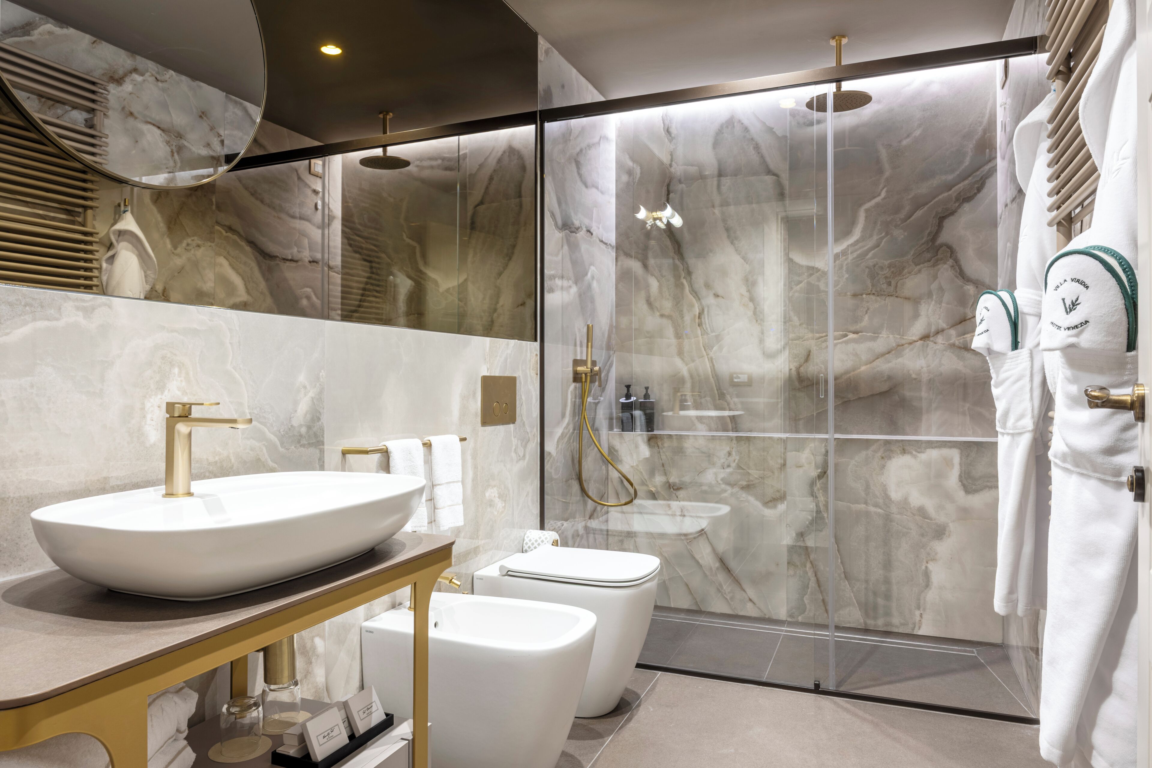 Een moderne badkamer met een groot marmeren wastafel, een toilet en een douchecabine met glazen wanden.
