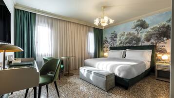 Quarto de hotel com cama, escrivaninha, cadeira, mesinha e um quadro na parede.
