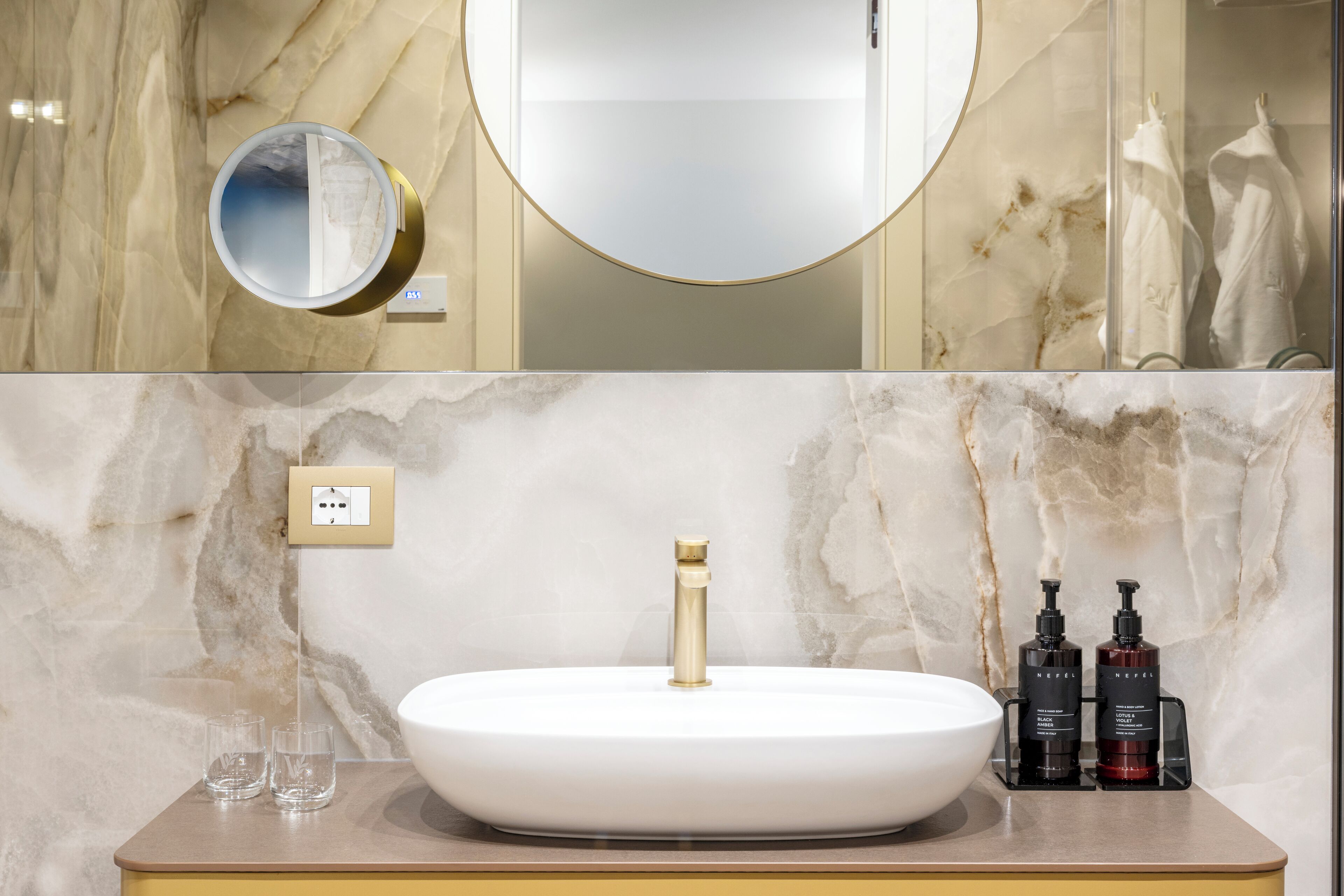 Un baño con lavamanos blanco, grifo dorado y dos artículos de tocador negros.
