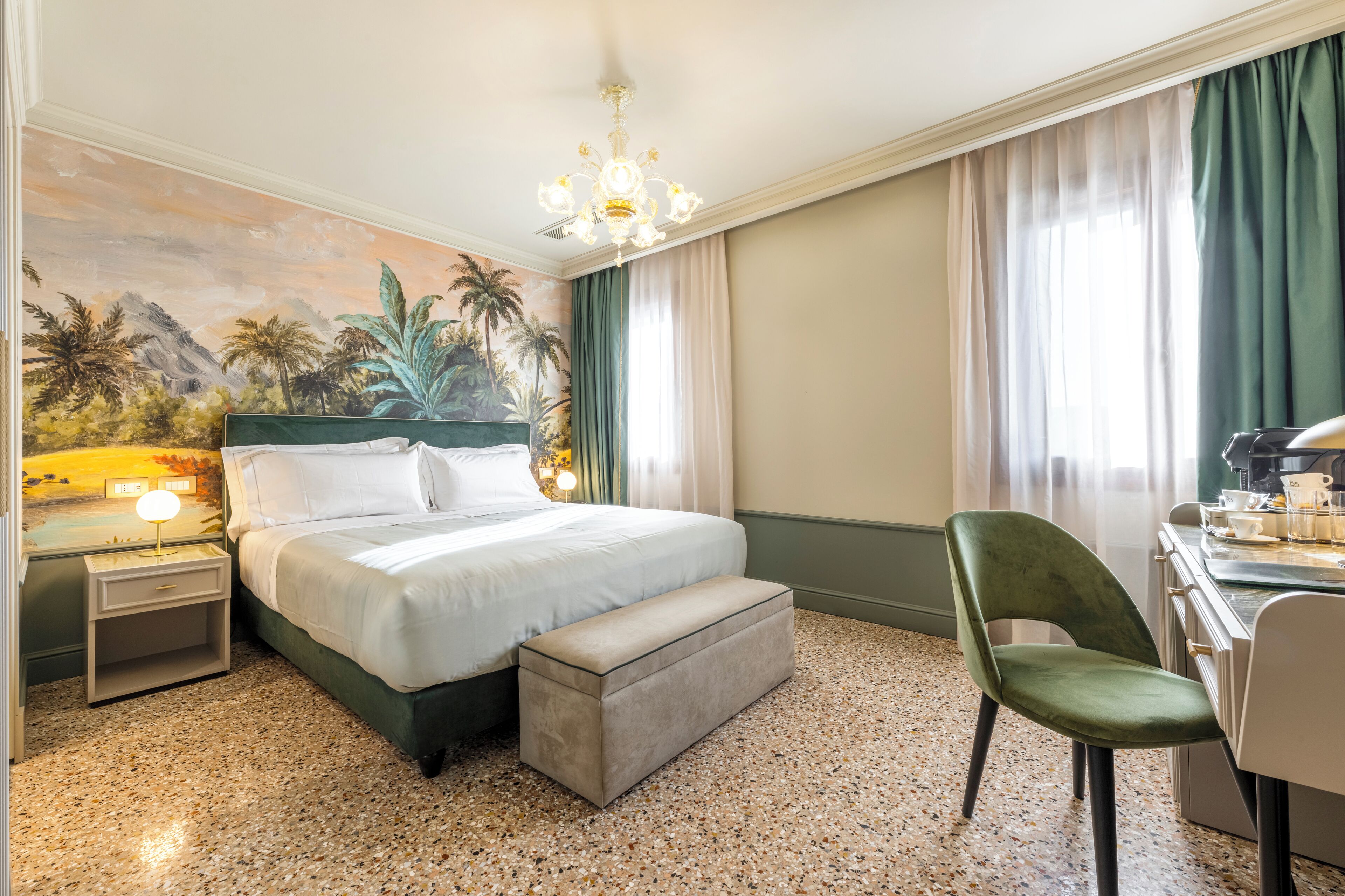 Una habitación de hotel con cama, escritorio, silla, mesita de noche, lámpara y un mural en la pared.
