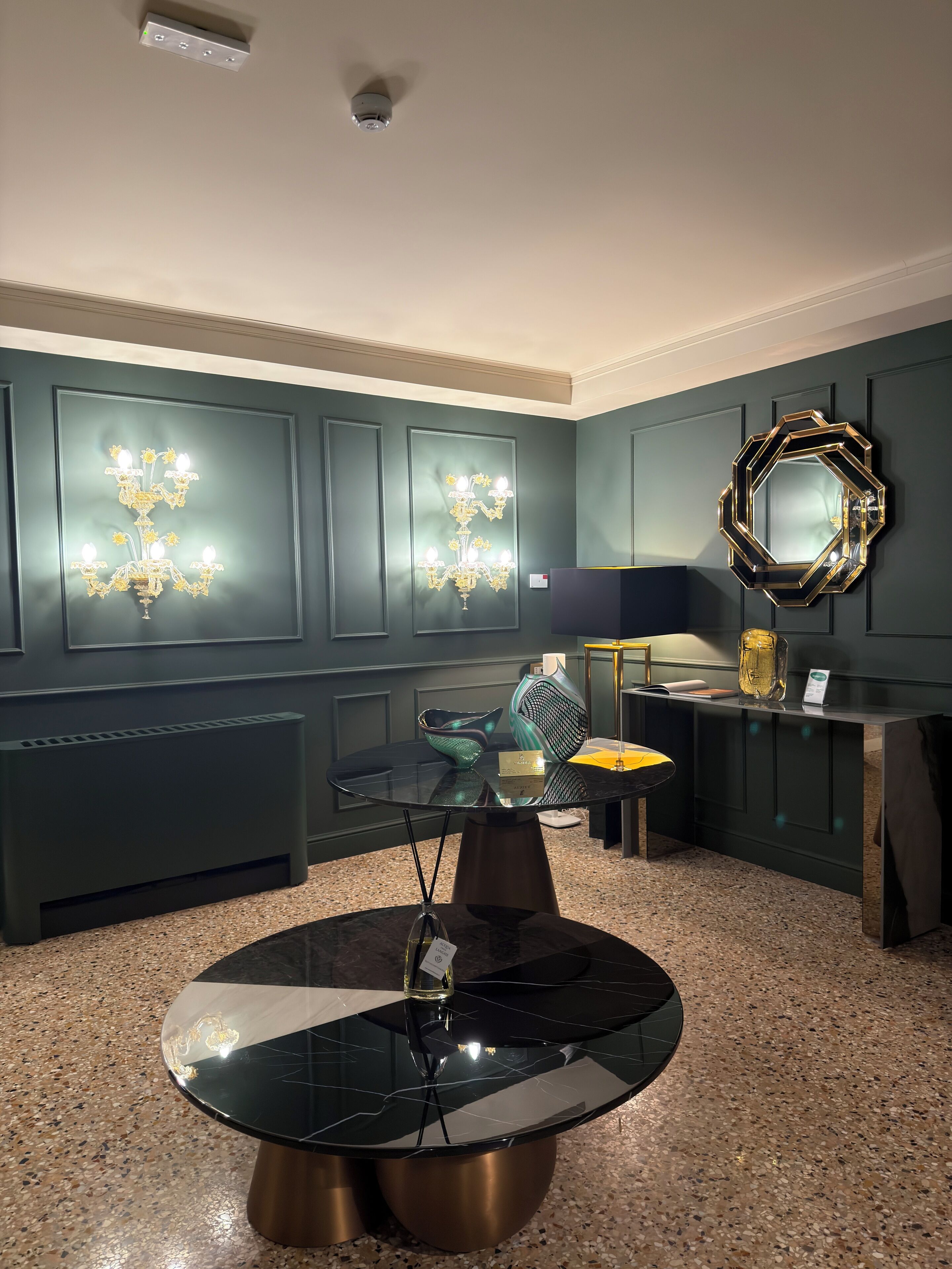 Un intérieur moderne avec une table ronde en verre, des murs vert foncé et des luminaires décoratifs.