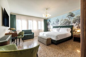 Ein Hotelzimmer mit Bett, Schreibtisch, Stuhl, Fernseher und einem Bild an der Wand.