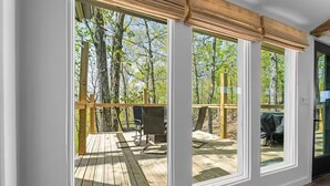 Una habitación con amplios ventanales que dan a una terraza de madera con mobiliario exterior.