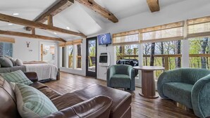 Una sala de estar amplia con techo alto, vigas de madera, ventanas grandes, chimenea y televisor.