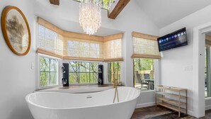 Un baño moderno con una bañera independiente grande, detalles de madera y un amplio ventanal con vistas al exterior.