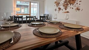 Uma sala de jantar com uma mesa de madeira posta para seis pessoas, um mapa-múndi na parede e uma luminária pendente moderna.