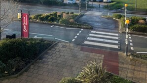 Un'area di parcheggio con uno striscione rosso con la scritta "Southsea", un attraversamento pedonale e vista sul mare e su un faro in lontananza.