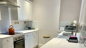 Una cucina moderna con mobili bianchi, forno integrato, bollitore e un piccolo bancone con sgabelli.