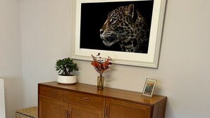 Una stanza con un armadio in legno, un quadro incorniciato con un leopardo, una piccola pianta in vaso e un vaso con fiori.