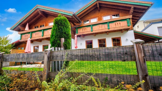 A traditional chalet with a wooden facade, a sloped roof, and a balcony with a pink umbrella. - Feriendorf Wildschonau With Private Garden (Wildschönau)
