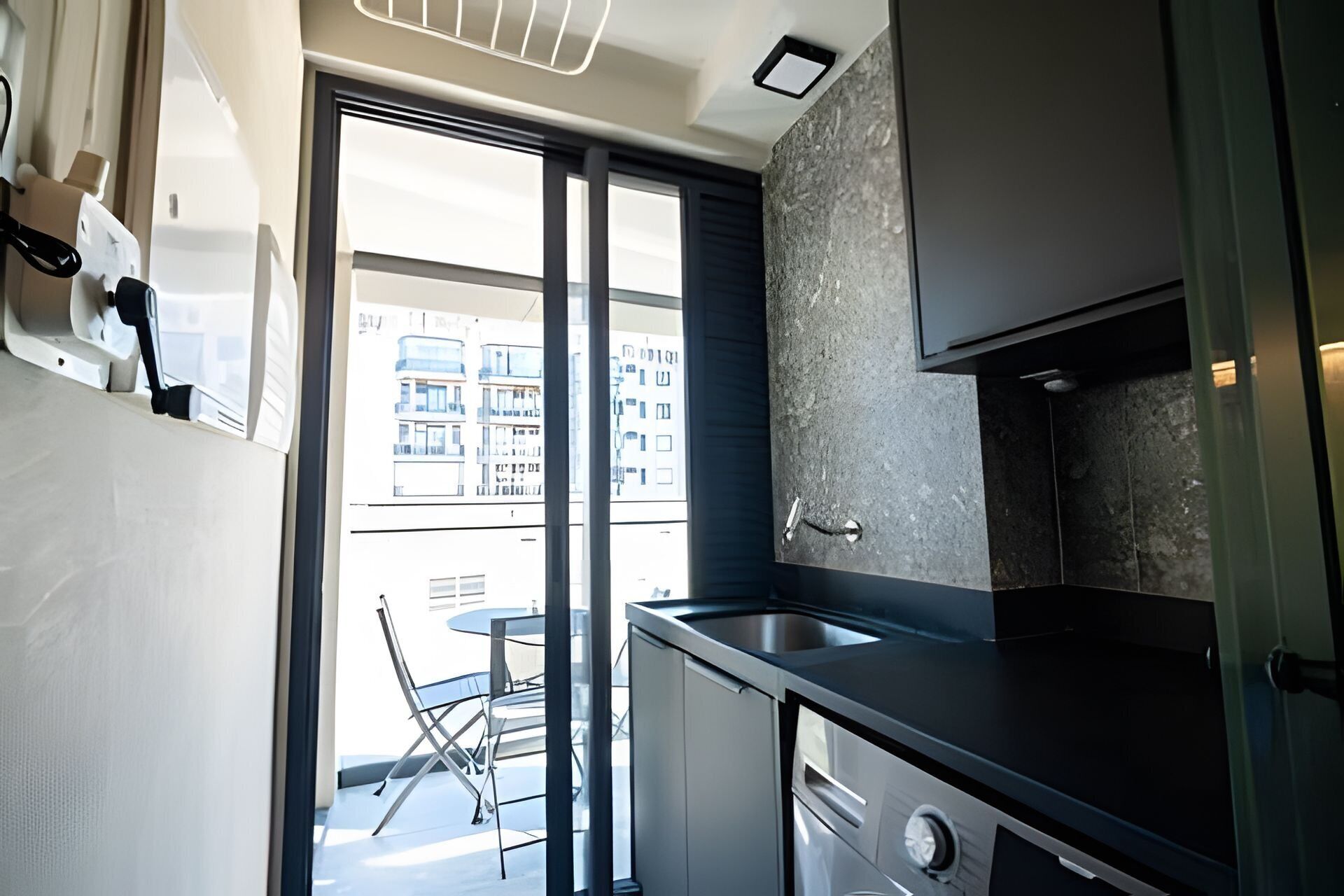 A modern kitchen with a large window, a dining area with a table and chairs, and a view of buildings outside.