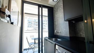A modern kitchen with a large window, a dining area with a table and chairs, and a view of buildings outside.