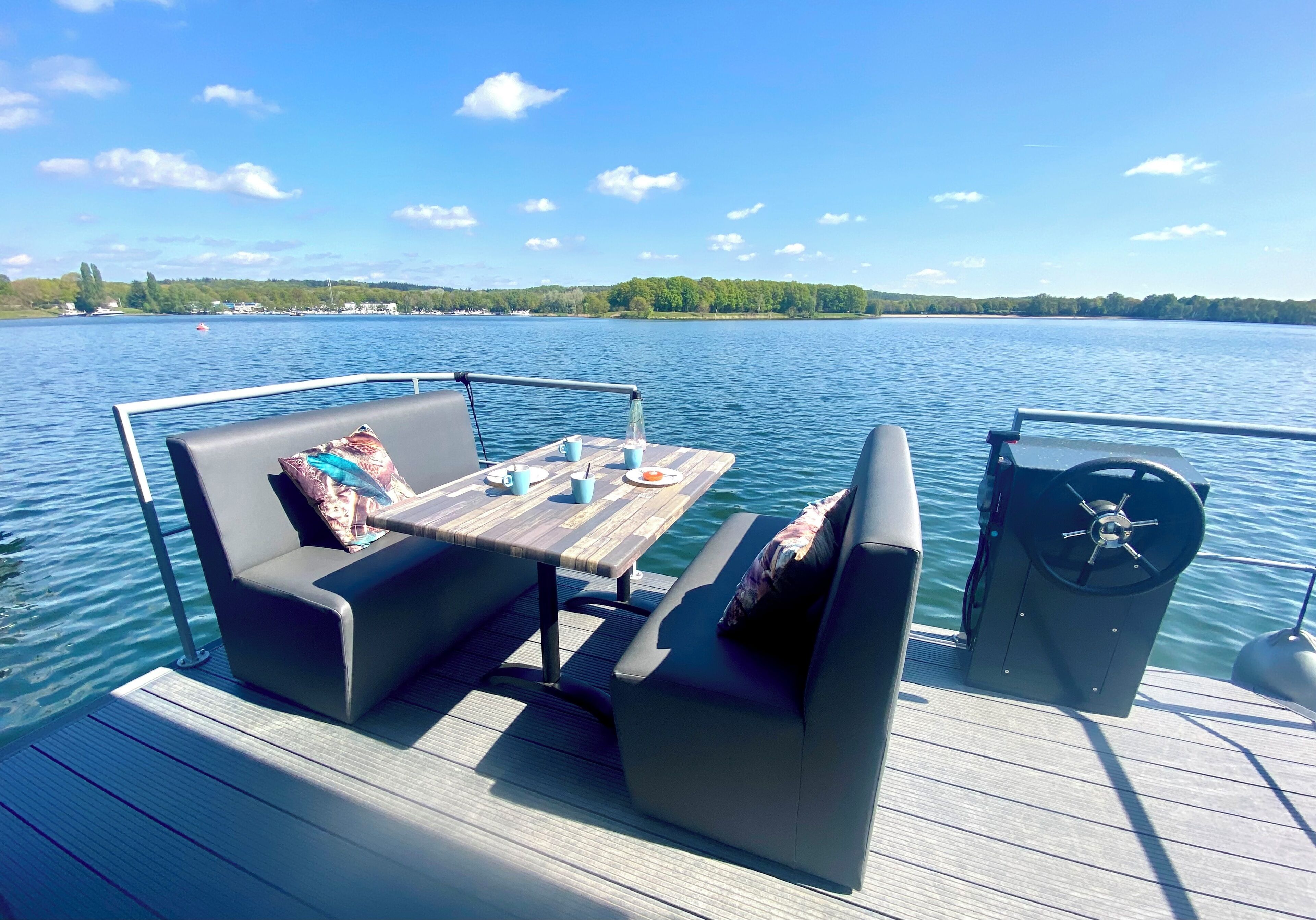 Une terrasse avec une table et deux canapés, un volant et une vue sur un lac bordé d’une forêt.