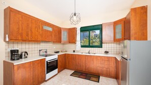 Een keuken met houten kastjes, een fornuis, een koelkast en een raam met groene omlijsting.