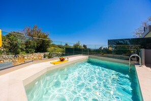 A swimming pool with clear water, surrounded by a stone wall and greenery.