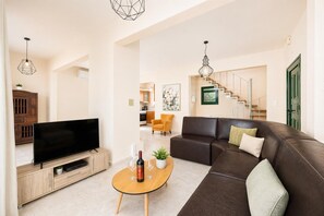 A modern living room with a flat-screen TV, leather sofa, wooden coffee table, and a staircase leading to an upper floor.