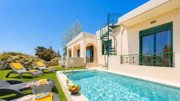A pool area with lounge chairs, a small table with a bottle and fruit, and a building with a spiral staircase.