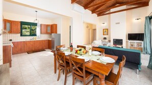 A modern kitchen with wooden cabinets, a dining table set for four, and a living area with a TV and seating.