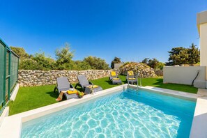 A swimming pool with two lounge chairs and a stone wall.