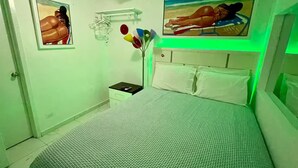A bedroom with a bed, a nightstand, a wall-mounted shelf, and a painting.
