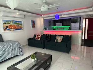 Una sala moderna con un conjunto de sofá, una mesa de centro y una cocina con una encimera iluminada con neón.