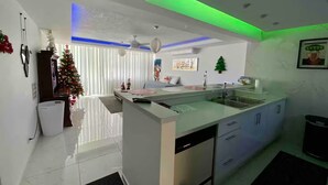 A modern kitchen with a central island, white cabinetry, and a green under-cabinet lighting.